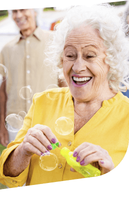 Joyful Elderly Woman Blowing Bubbles Outdoors with Friends in Independent Living Joyful Elderly Woman Blowing Bubbles Outdoors with Friends in Independent Living