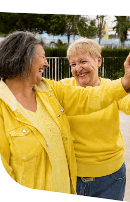 Two Elderly Women Embracing and Laughing Together Outdoors at Independent Living Community Two Elderly Women Embracing and Laughing Together Outdoors at Independent Living Community