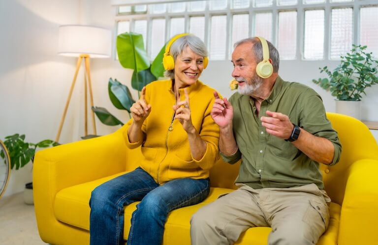 Elderly Couple Wearing Headphones and Enjoying Music on Couch at Independent Living Facility