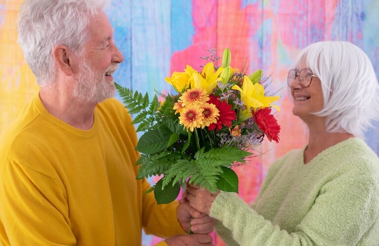Elderly Man Giving a Bouquet of Flowers to Smiling Woman in Independent Living