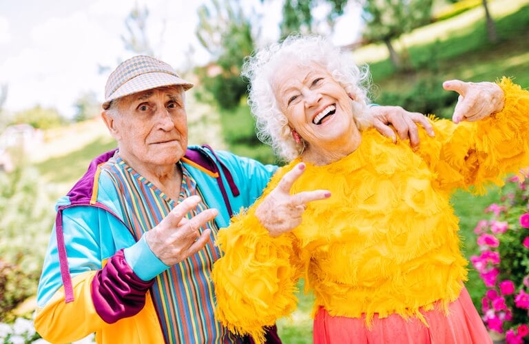 Playful Elderly Couple Posing in Colorful Outfits Outdoors at Independent Living Community