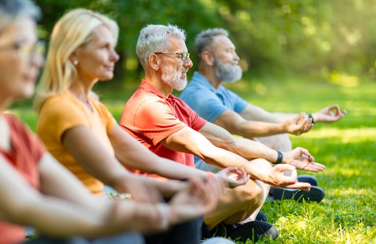 Group of Elderly Residents Meditating Outdoors on Grass in Independent Living