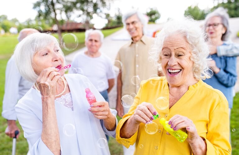 Elderly Women Blowing Bubbles Outdoors with Friends at Independent Living Facility