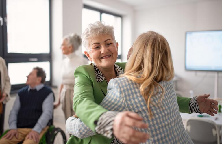 Smiling Elderly Woman Embracing a Friend During Group Activity at Independent Living Community