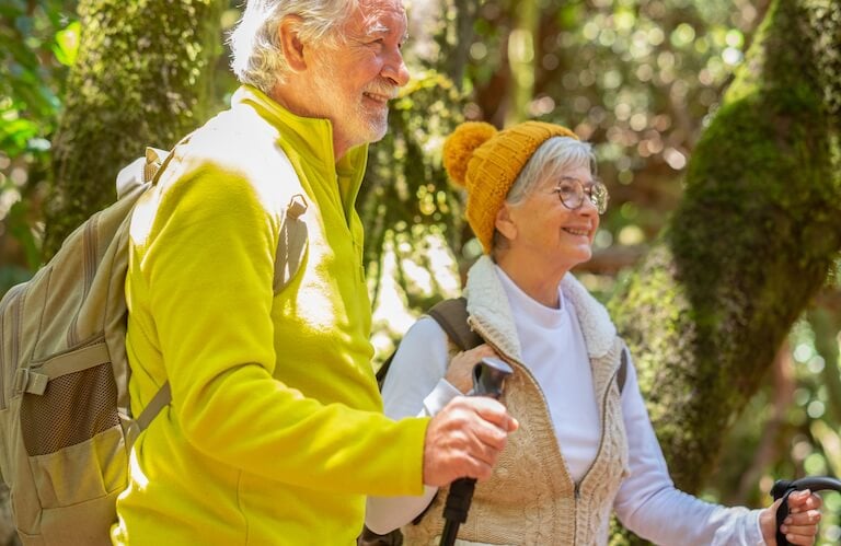 Elderly Couple Hiking with Backpacks and Poles Through Forest in Independent Living