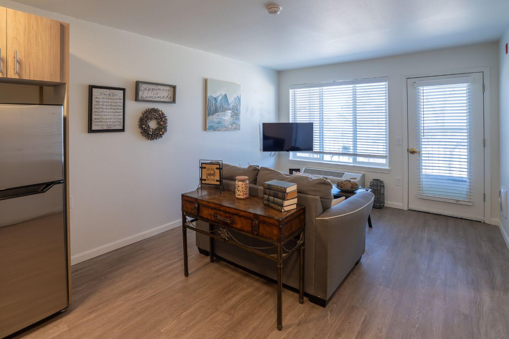 Open Apartment Living Room with Sofa, Television, and Patio Door in Our Independent Living Community