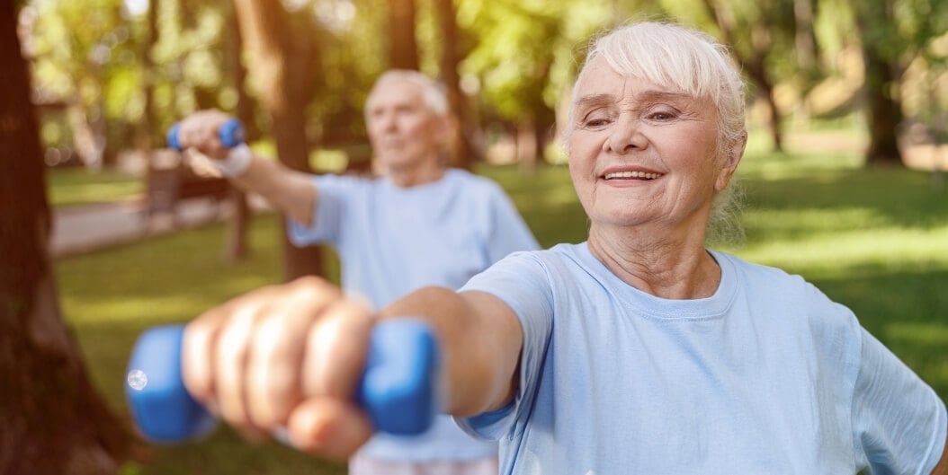 Smiling Elderly Woman Lifting Dumbbells in Sunny Park at Independent Facility